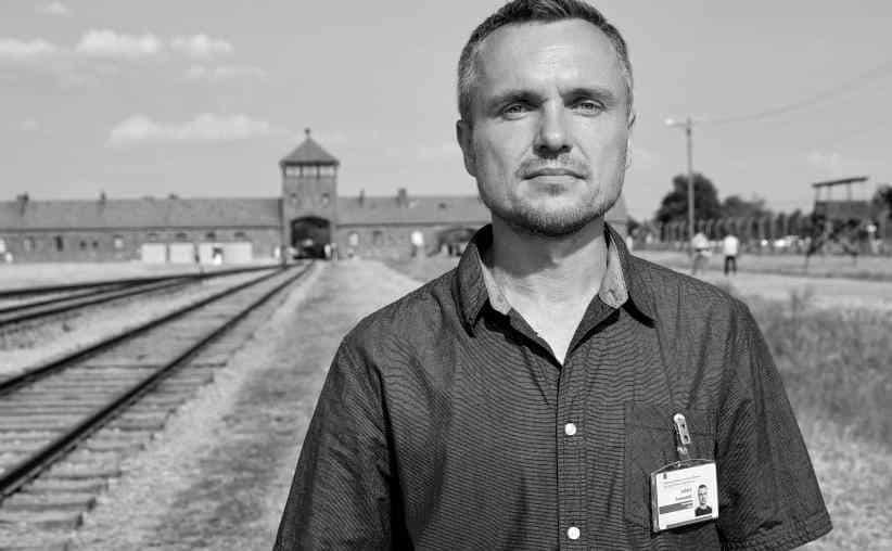 Guide with a badge in a dark shirt in front of Auschwitz II Birkenau gate