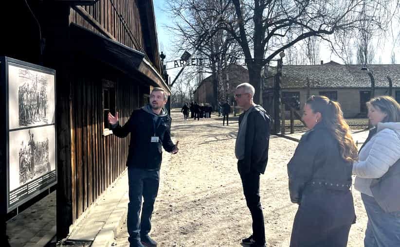 A guide with visitors in front of the main Auschwitz I gate Arbeit Macht Frei.