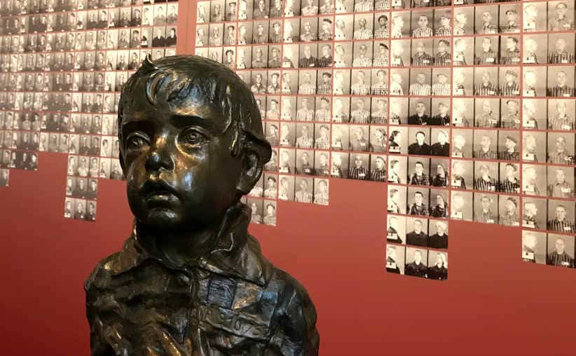 Bronze carving of a prisoner boy and registration photos on a red wall in Block 16: Czech national exhibition, Auschwitz I Main Camp.