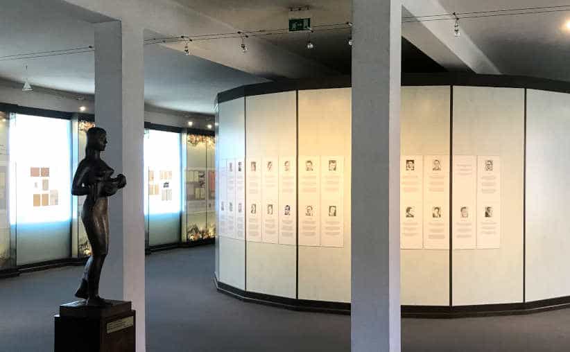 Bronze carving of a woman and photos with info on white boards in Block 16: Czech national exhibition, Auschwitz I Main Camp.