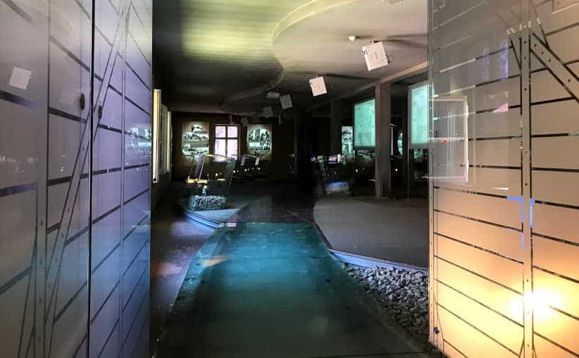 Inside of a glass rail track with glass path and projected info graphics in front in Block 18: Hungarian national exhibition, Auschwitz I Main Camp.