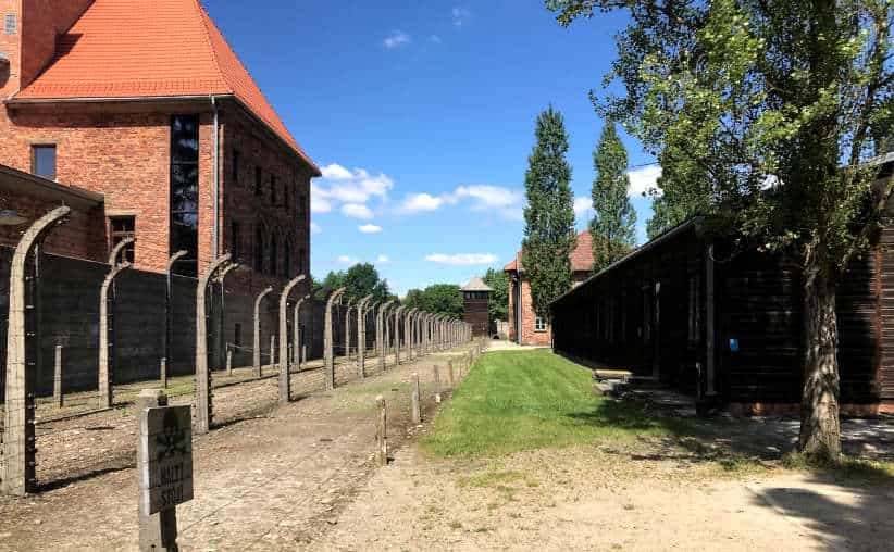 A large former theater used as a storage facility for Zyklon B, a barbed wire fence and a wooden laundry at the Auschwitz I main camp.