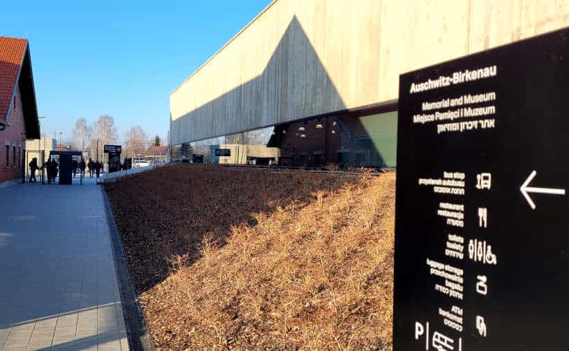 Info board with directions and visitors after the tour of Auschwitz I Main Camp exiting between the main reception on the left and the restaurant on the right.